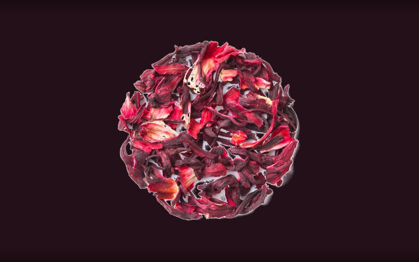 Dried hibiscus flowers and herbal tea leaves on a dark aubergine surface